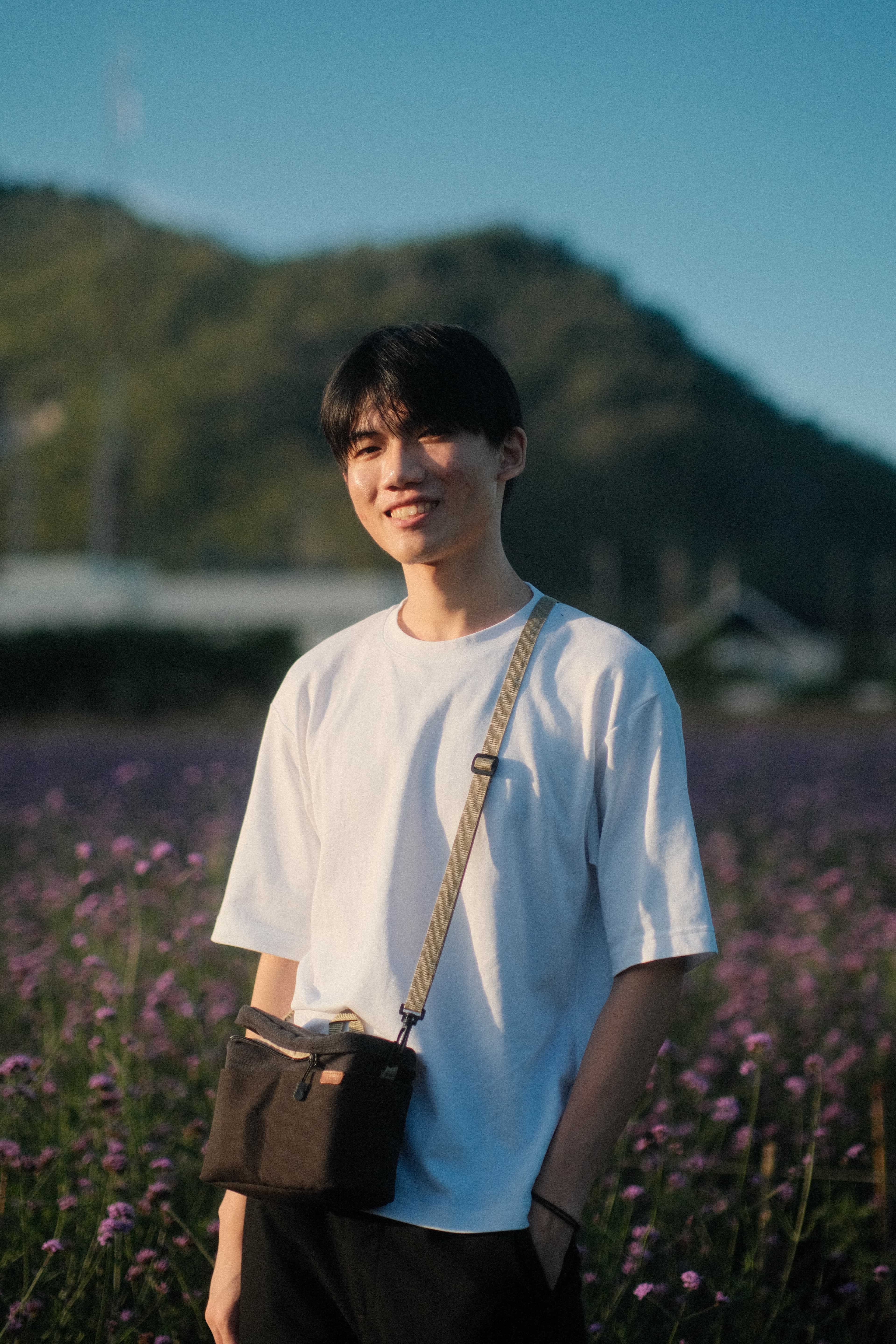 A man smiling in a white shirt with a crossbody bag.